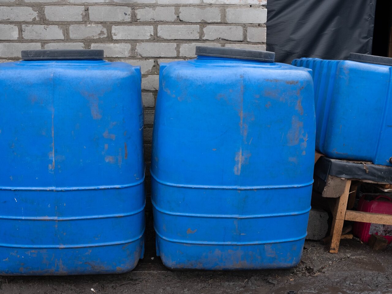 Three large blue plastic water tanks lined up against a brick wall outside a frontline house.