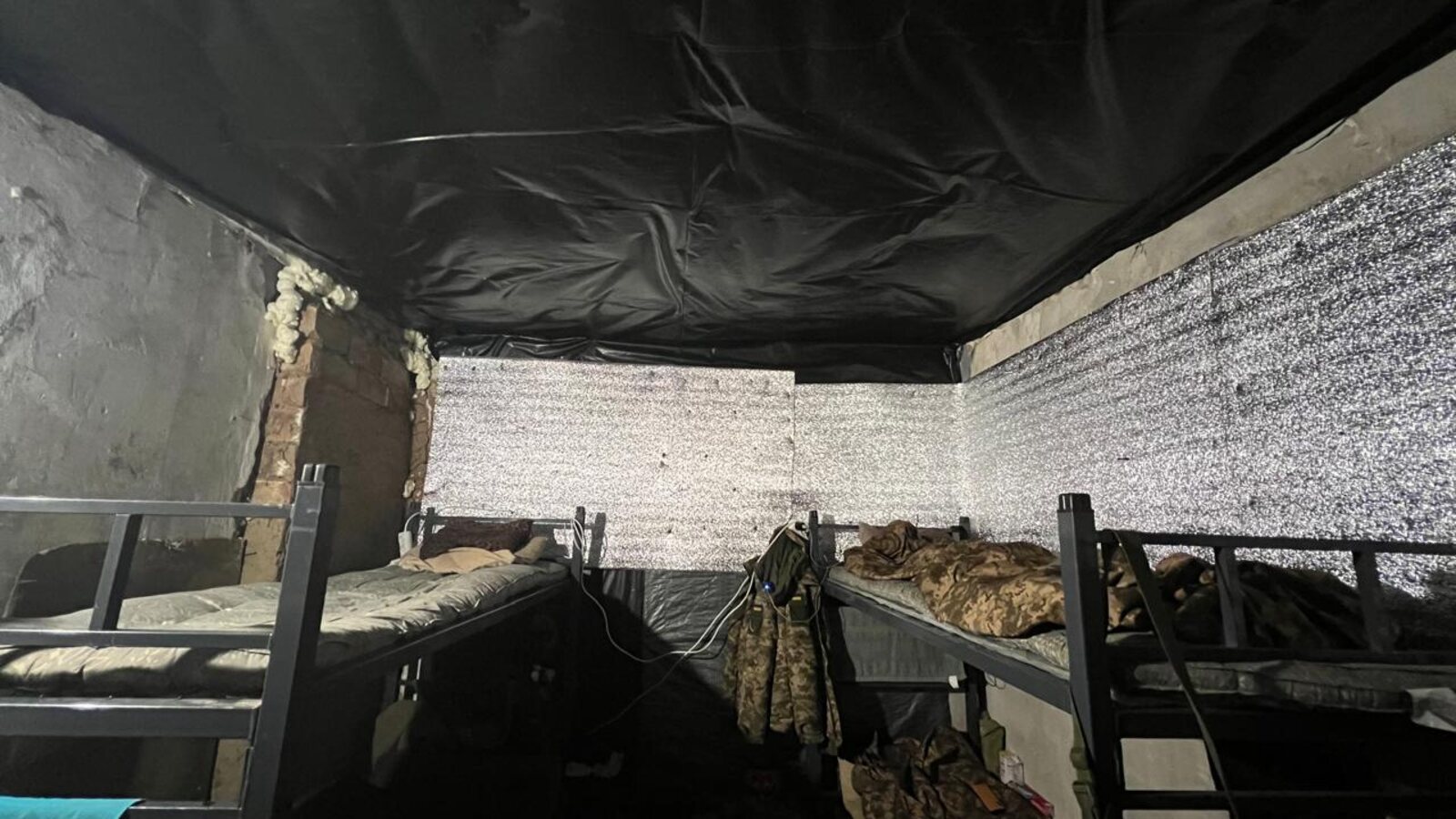 The interior of a restored frontline shelter — bunk beds with mattresses, insulated walls, weatherproof ceiling.